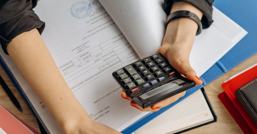 A business professional uses a calculator among documents and laptop on a desk for financial tasks.